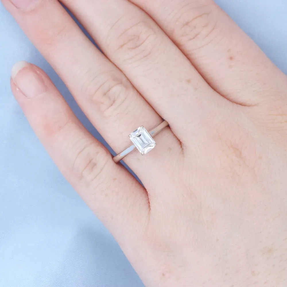 Emerald-cut solitaire engagement ring modeled on a hand