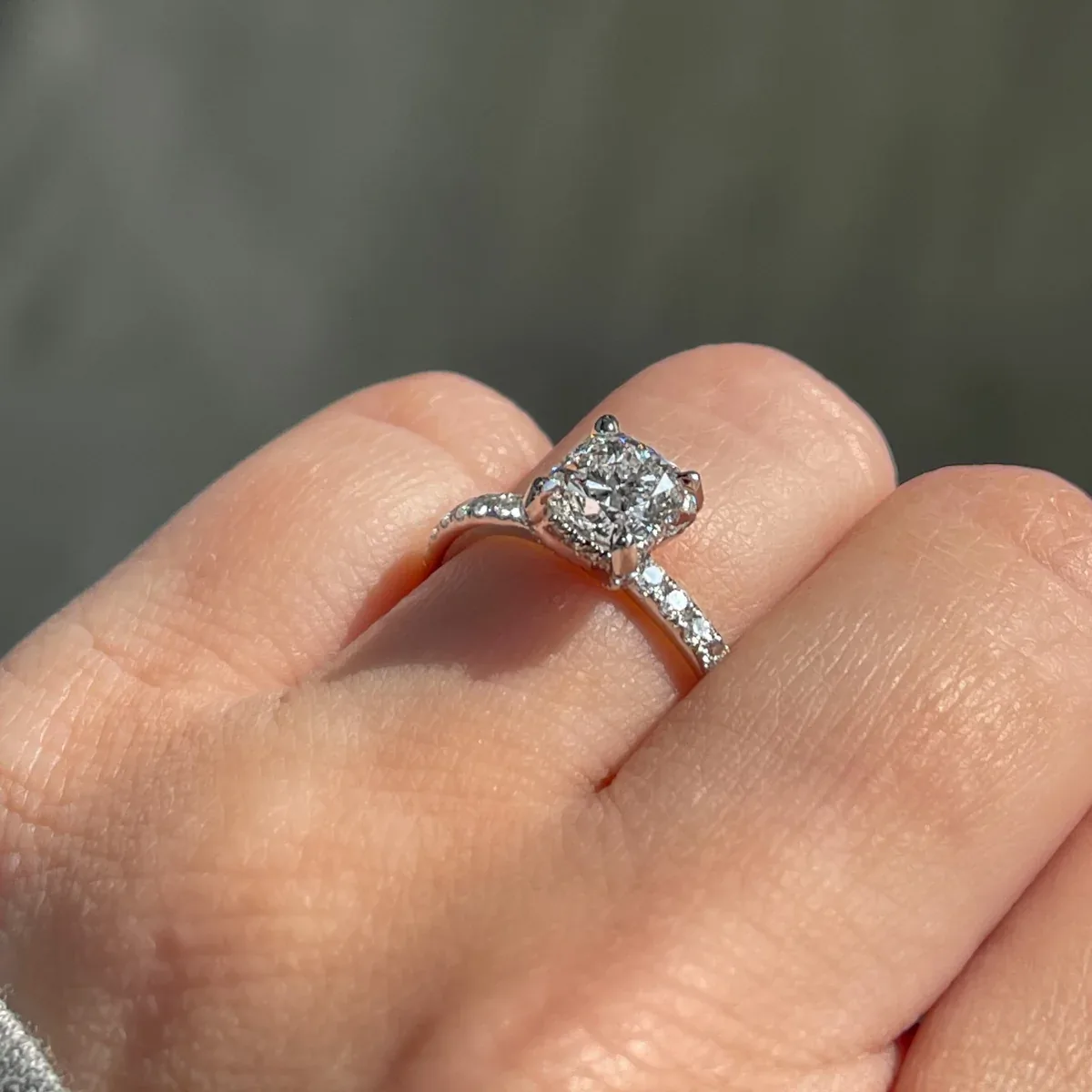 Cushion diamond engagement ring with a hidden halo and pave band modeled on a hand
